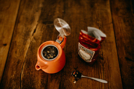 an orange teapot next to a tea bag and a spoon