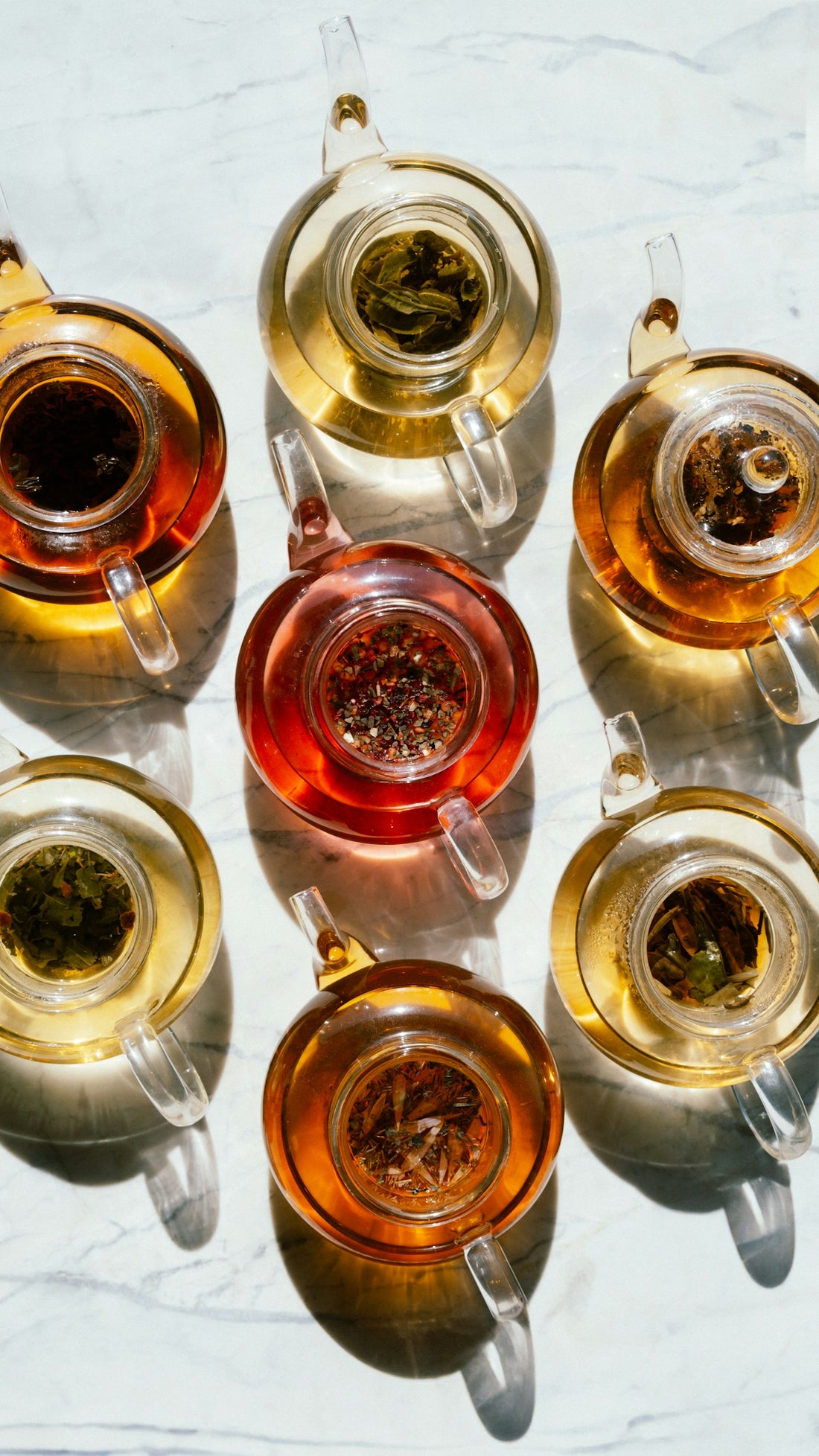 Several glass teapots filled with various teas.