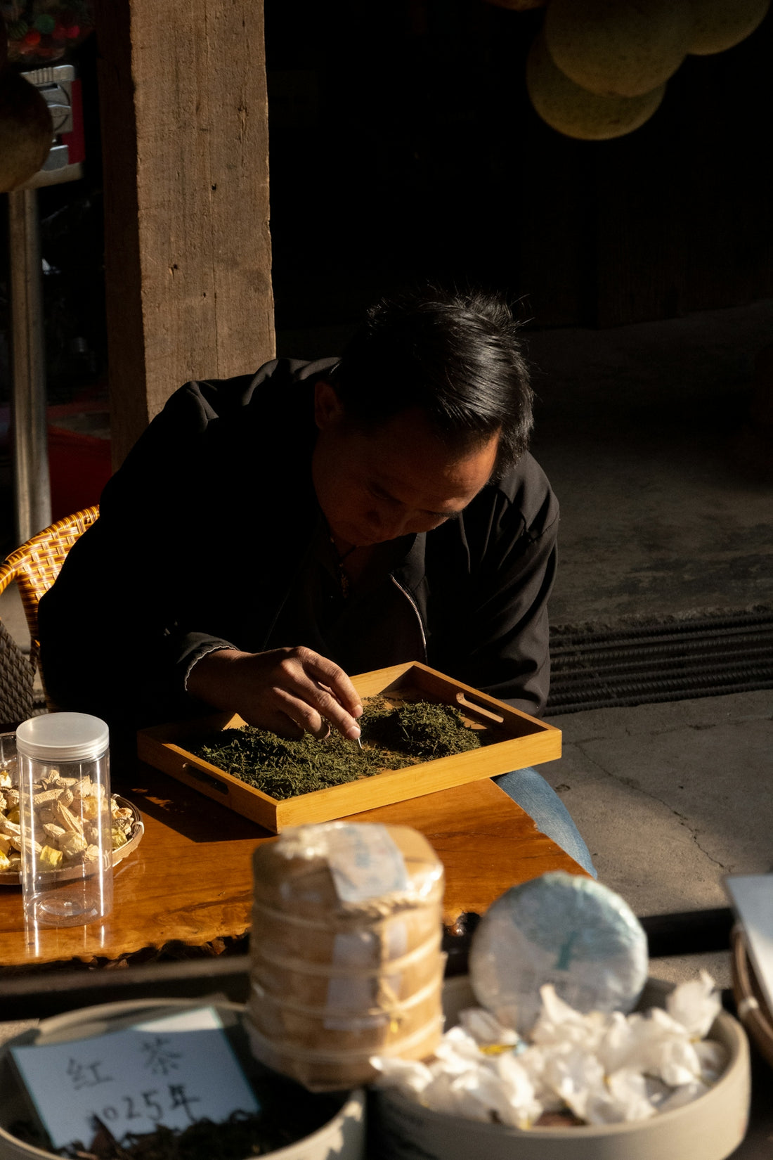Man sorting green tea leaves on a wooden tray