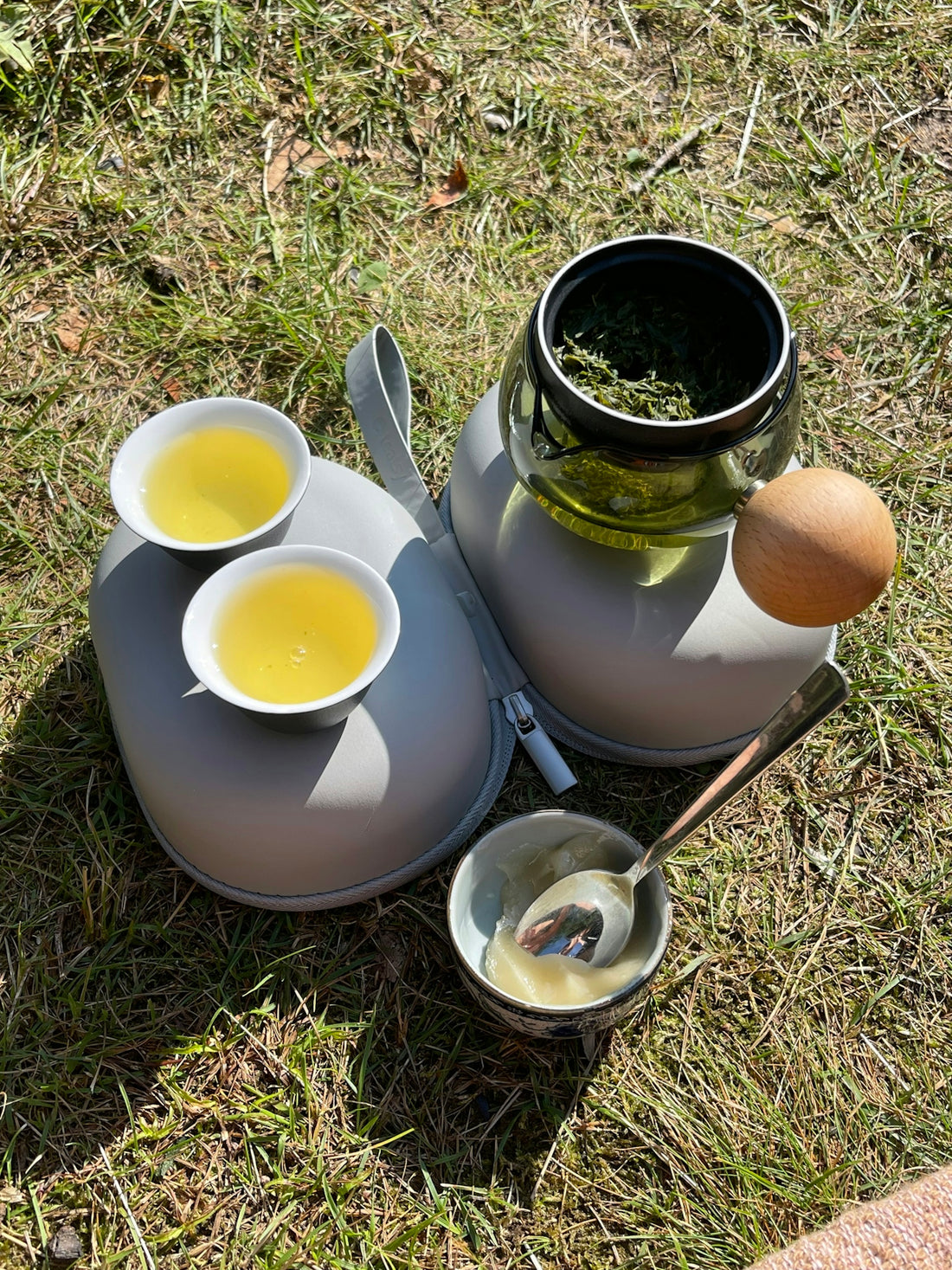 Two cups of tea and a teapot on grass outdoors.