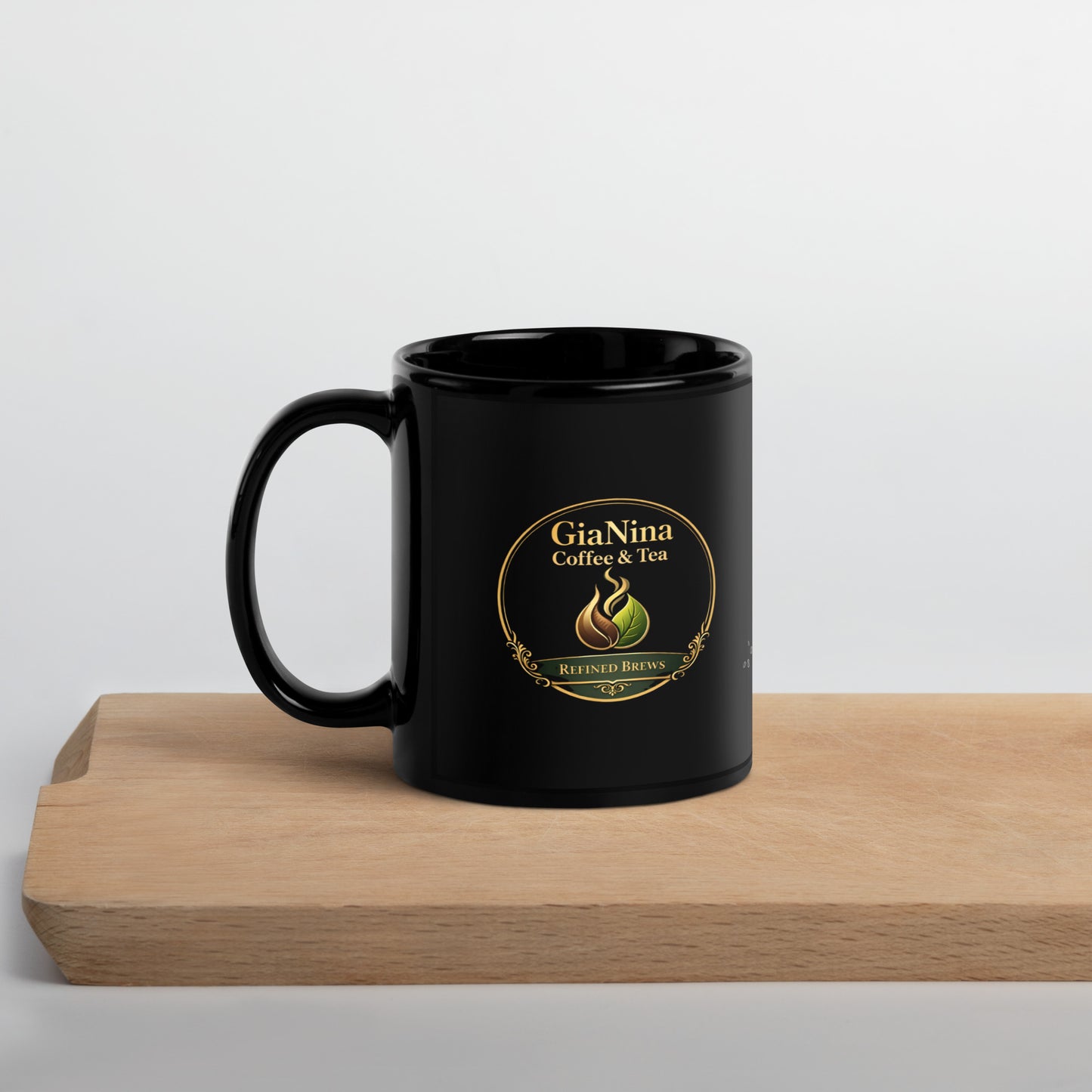 A glossy black ceramic coffee mug with a gold and green GiaNina Coffee & Tea logo, resting on a light wood cutting board against a neutral light gray background.