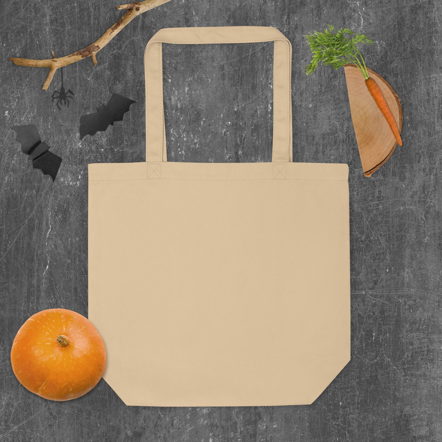 Beige tote bag on a dark gray background with a pumpkin, carrot, and decorative elements.