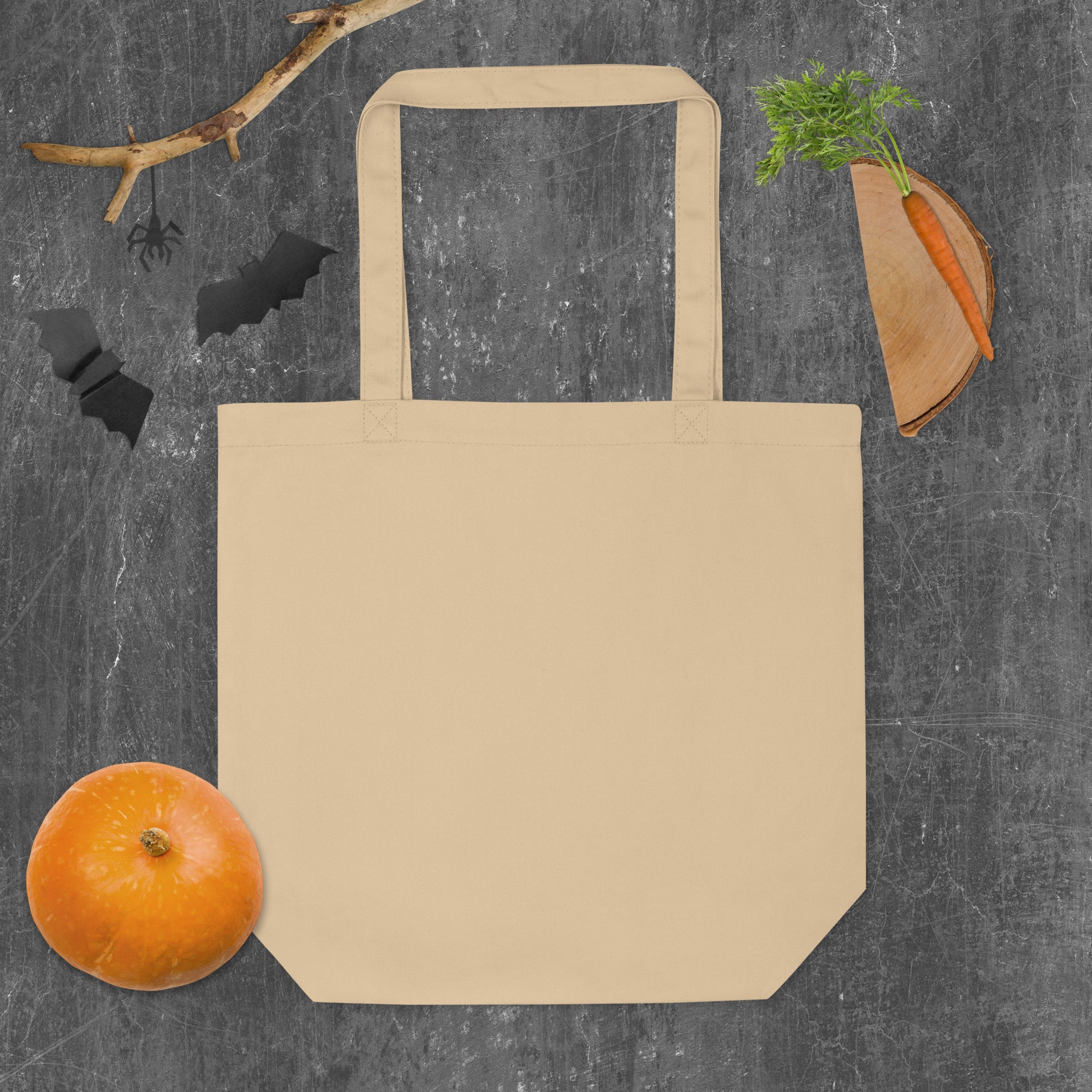Beige tote bag on a dark gray background with a pumpkin, carrot, and decorative elements.