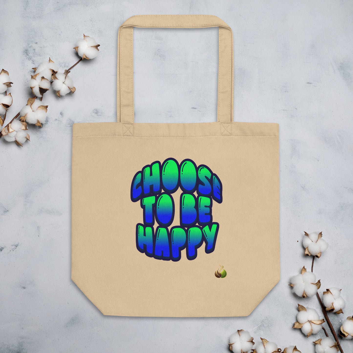 A beige canvas tote bag with the phrase 'CHOOS TO BE HAPPY' printed in a colorful 3D bubble font that gradients from green to blue. The bag is displayed on a light gray marble surface, styled with cotton bolls in the corners.