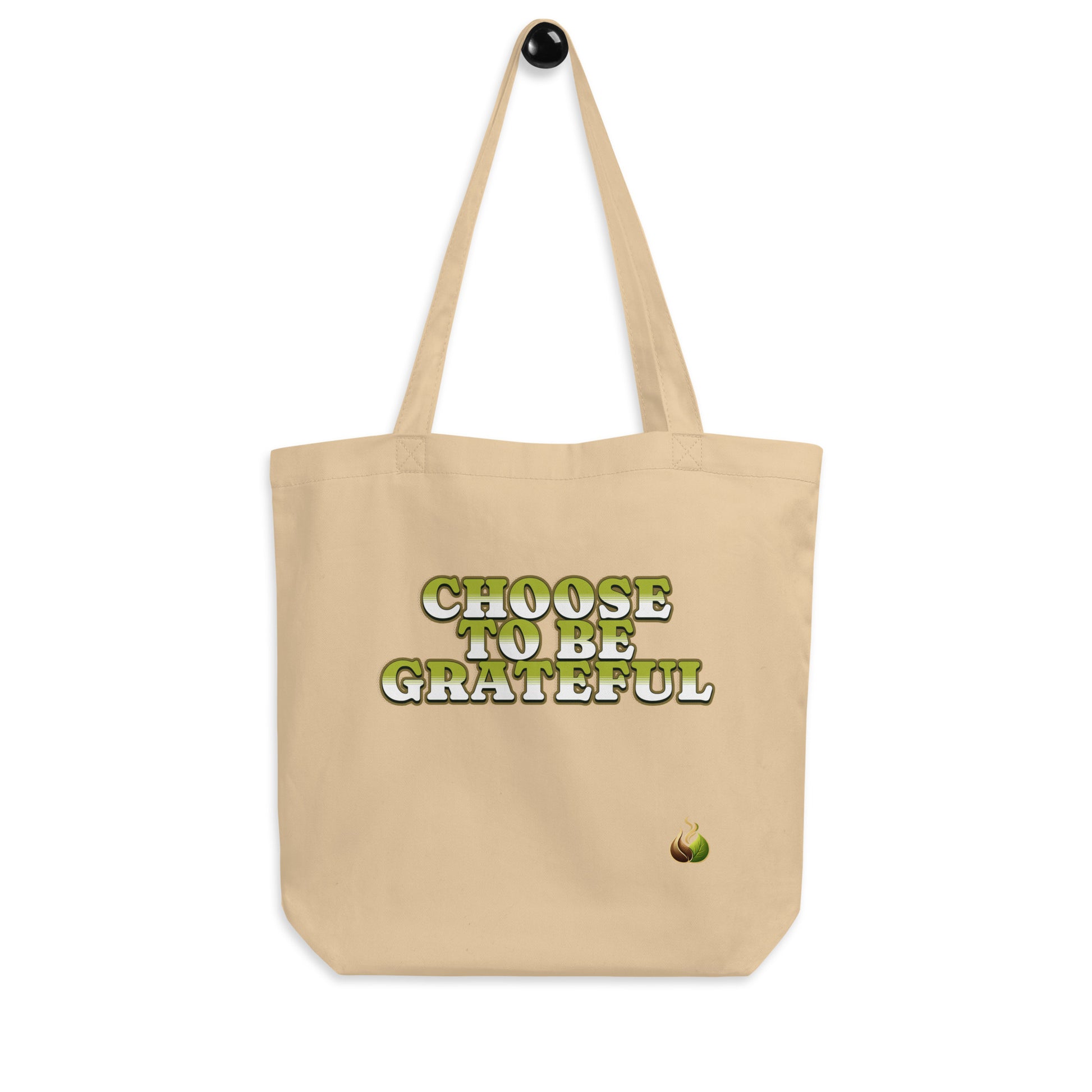 A beige canvas tote bag with two shoulder straps, featuring the printed text 'CHOOSE TO BE GRATEFUL' in green and white letters on the front, with a small green graphic near the bottom right corner.